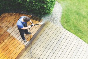 man cleaning terrace with a power washer - high water pressure cleaner on wooden terrace surface. Pressure washing metairie
