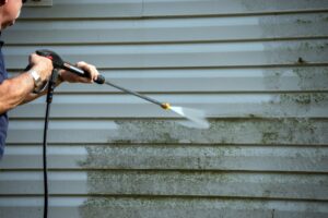 A man uses a power washer to clean mold off the siding of a house - pressure washing metairie